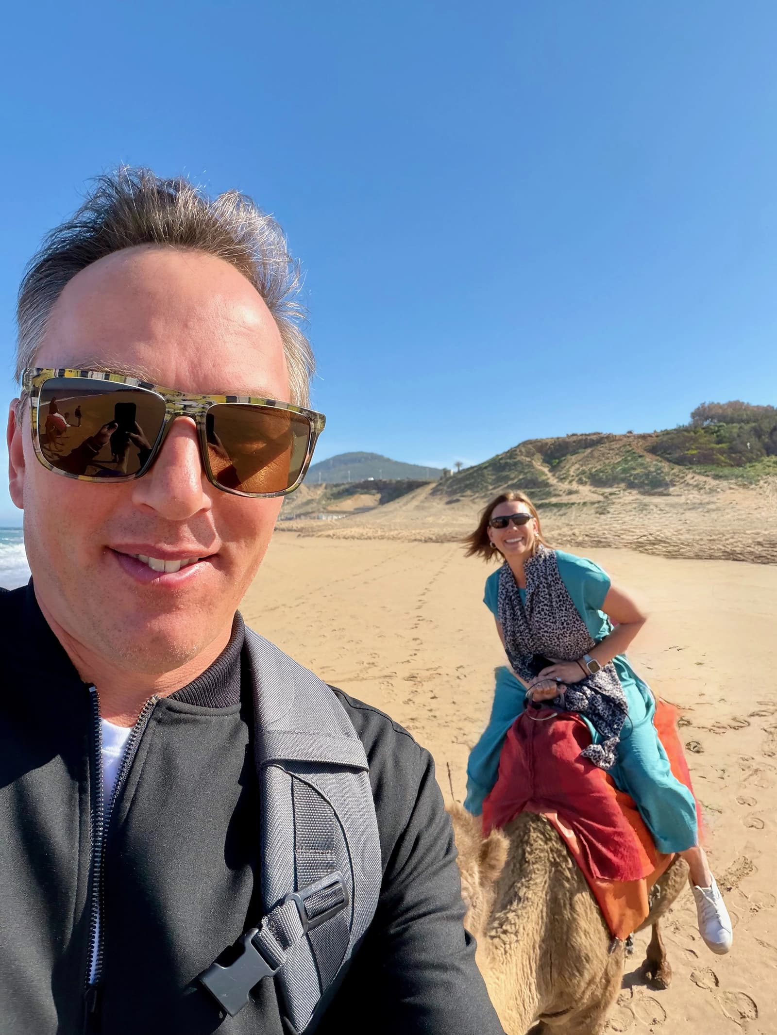 Jen and Kevin riding camels on a beach in Tangier