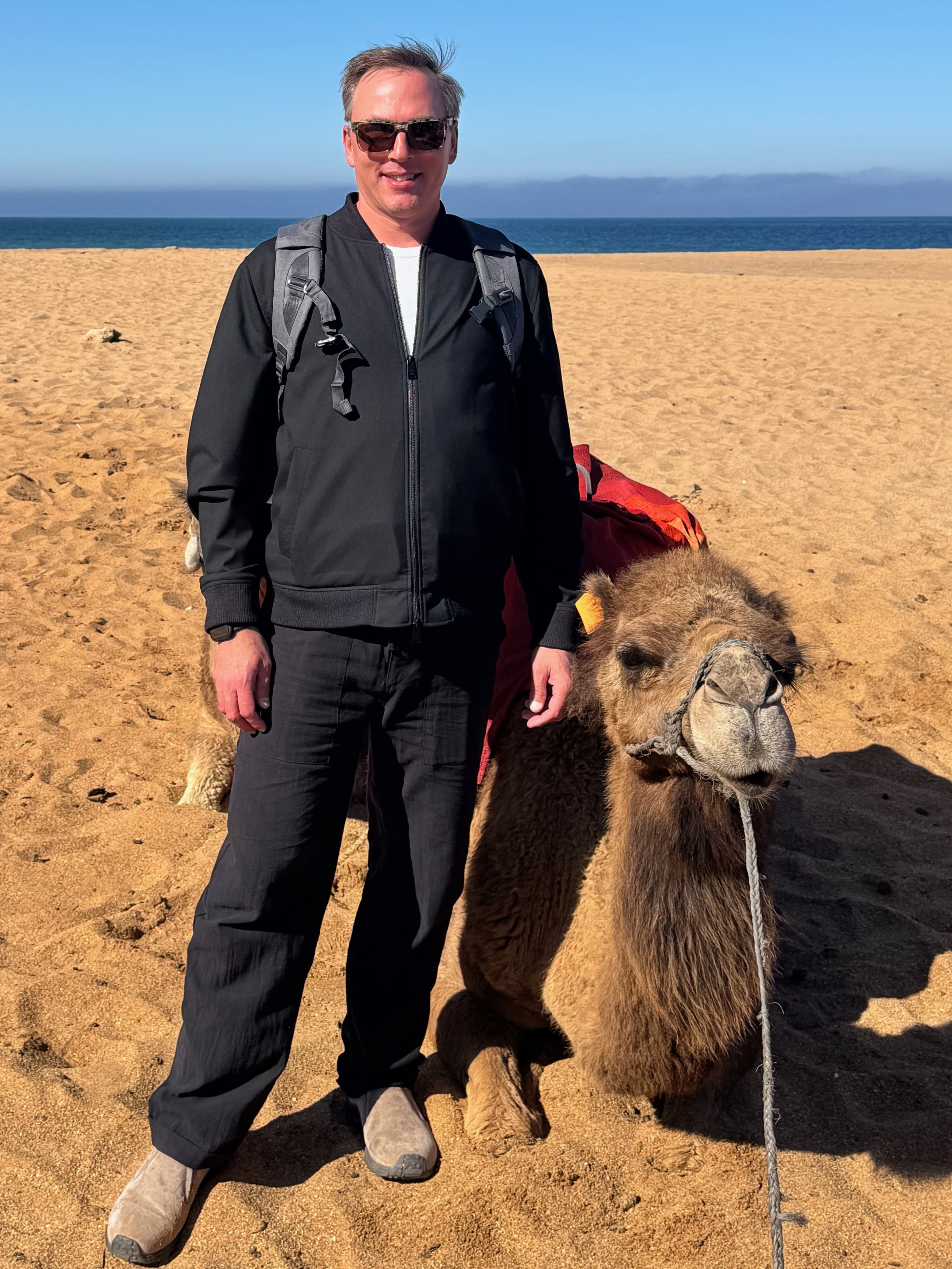 Kevin standing beside a camel on a beach in Tangier, Morocco